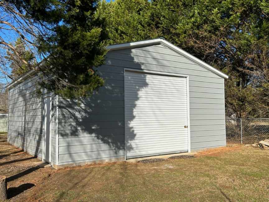 A white garage with a door open in the middle of a field.