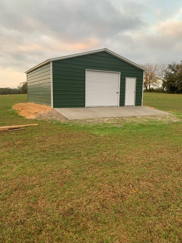 A green garage with two doors in the middle of an empty field.